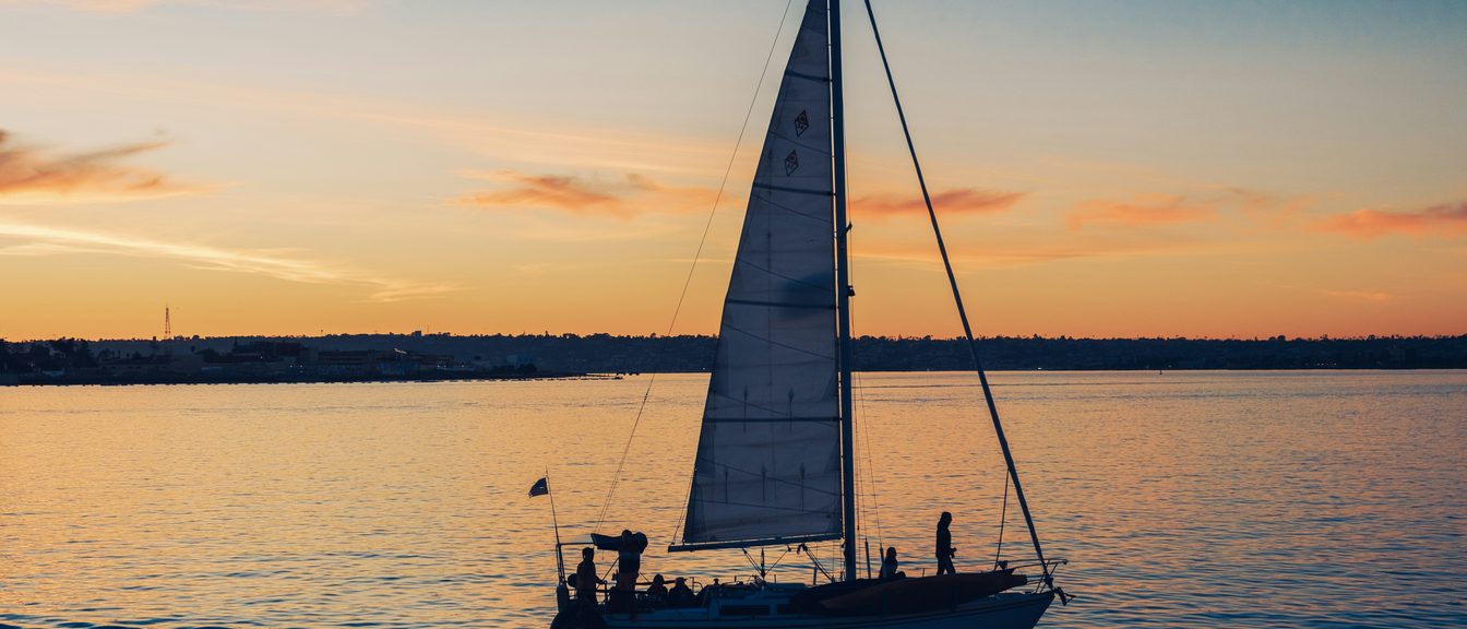 A sailboat at the helm on open water at golden hour
